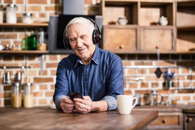 坐着快乐的老人一边用他的智能手机一边听音乐室内老年人成熟