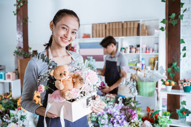 成人快乐的女人拿着礼品包装准备出售在花店工作时穿着围裙和朋友站在一起花卉室内生活方式