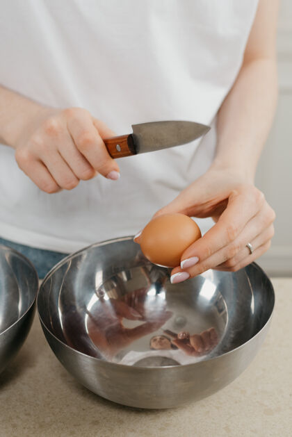 手工厨房不锈钢碗上方 一名年轻女子用刀打碎蛋壳的照片面包房鸡蛋刀