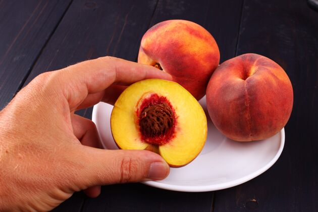 桃子把桃子放在一个盘子里 放在一个深色的木头表面上生的整个新鲜