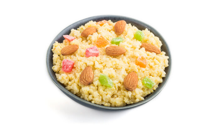 配料小米粥与蜜饯水果和杏仁在蓝色陶瓷碗隔离在白色的表面饮食盘子干燥