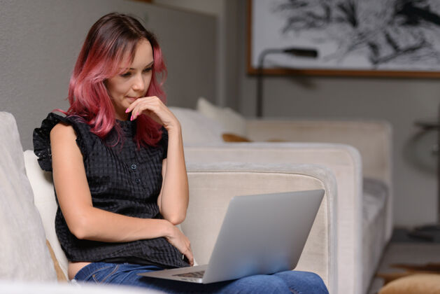 现代美丽的商人肖像与粉红色的头发使用笔记本电脑在客厅从家办公的概念室内家具数码