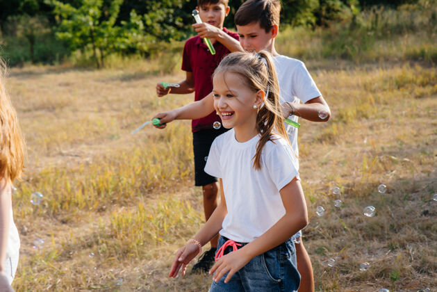 露营一大群兴高采烈的孩子在公园里玩 吹肥皂泡在儿童营里玩游戏活跃户外男孩