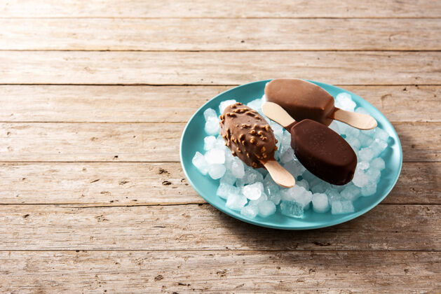 果汁巧克力冰棒和碎冰放在木桌上的蓝色盘子上冷藏自制水果