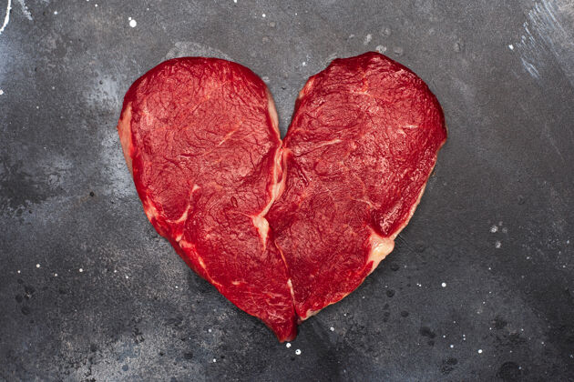 食物心形生鲜肉牛排 深色表面 顶视图生的心烧烤