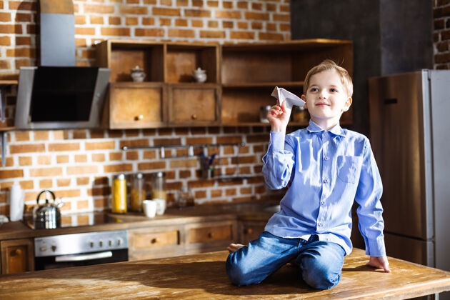房子高兴的小男孩坐在厨房里玩纸飞机积极智力快乐