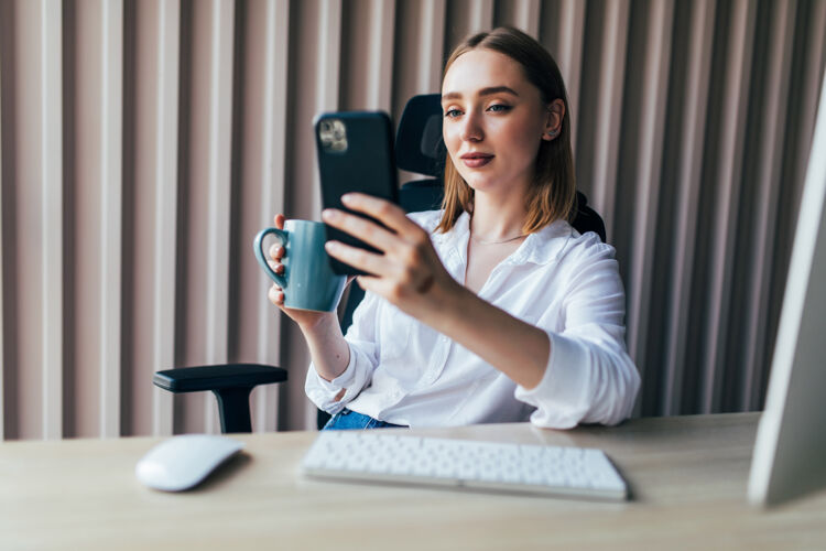 阅读年轻漂亮的女人在办公室的桌面上用电脑和手机上网员工视频传输