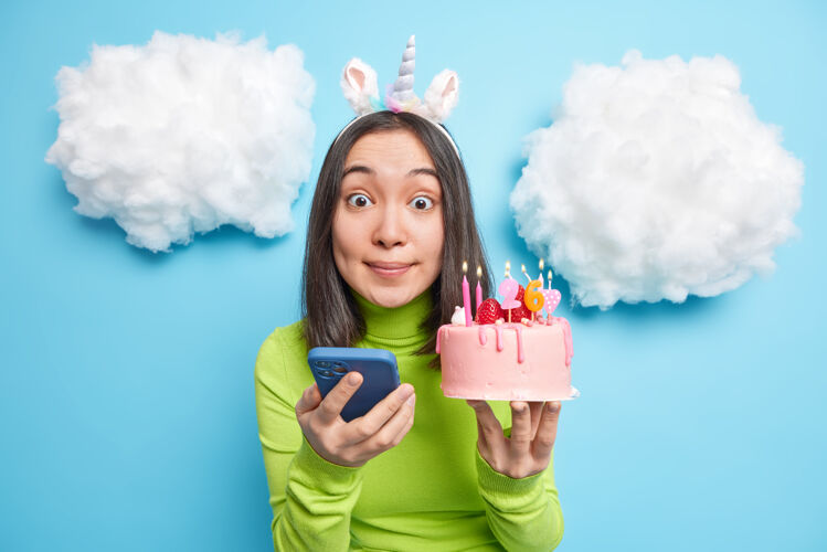 姿势女孩喜欢在社交网络上发布生日派对照片拿着蛋糕点着蜡烛看起来穿着休闲服就被蓝色隔离手机格子在线