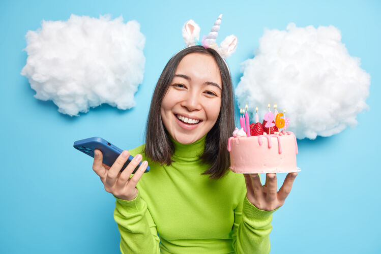 马球衫女人拿着生日蛋糕和智能手机设备微笑着牙齿高兴地接受祝贺她26日的蓝色姿势庆祝蛋糕生日