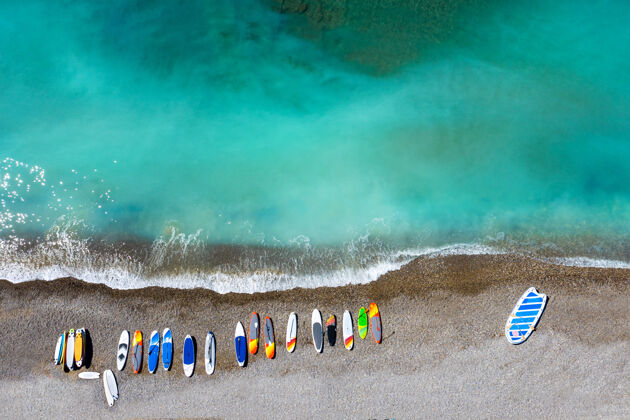 顶视图五颜六色的冲浪板杂乱无章地躺在瓦片海滩上的俯视图海洋冲浪板夏天