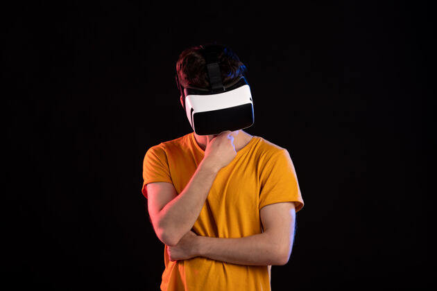 耳机戴着虚拟现实耳机的年轻人在黑暗的游戏视频d的正面视图年轻人喜剧演员穿