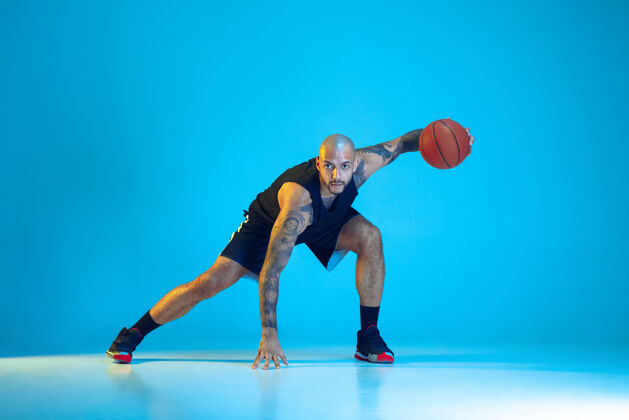 健身年轻的篮球队员穿着运动服训练 在运动中练习 在霓虹灯下的蓝色背景下孤立运动运动的概念 运动 活力和活力 健康的生活方式运动员冠军篮球