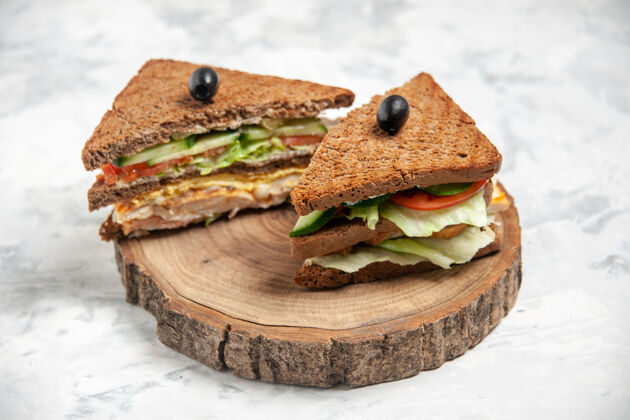 板特写镜头的美味三明治黑面包装饰橄榄木砧板上的染色白色表面与自由空间橄榄小吃染色
