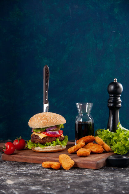 食物刀在肉三明治和鸡块番茄干胡椒在木板酱番茄酱在深蓝色的表面番茄酱晚餐板