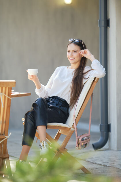 女人阳光明媚的日子里 快乐的年轻女子坐在咖啡馆的露台上喝酒咖啡女人在户外享受春天的第一缕阳光可爱坐着人