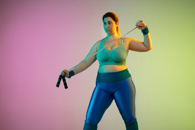 锻炼年轻白种人大码女模特在霓虹灯下的渐变紫绿色墙壁上训练身体体育健身