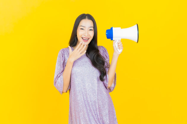 公告年轻的亚洲女人用黄色的扩音器微笑沟通发言人墙