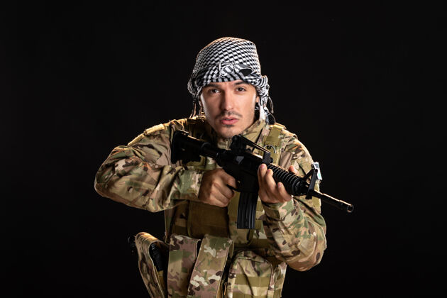 军人身穿迷彩服的巴勒斯坦士兵在黑墙上用机关枪战斗肖像战斗制服