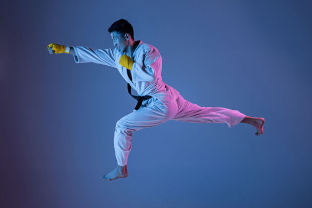 技能自信的韩国人穿着和服练习徒手格斗 武术年轻的男子拳击手在霓虹灯下用黑带在梯度背景上训练健康的生活方式 运动的概念战斗准备运动