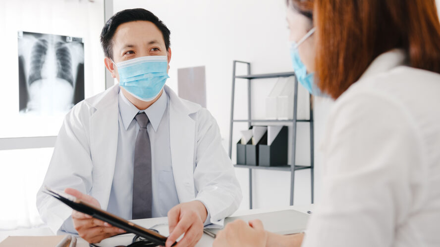 人员严肃的亚洲男医生戴防护口罩用平板电脑发表精彩的新闻谈话讨论结果疾病社交距离医生