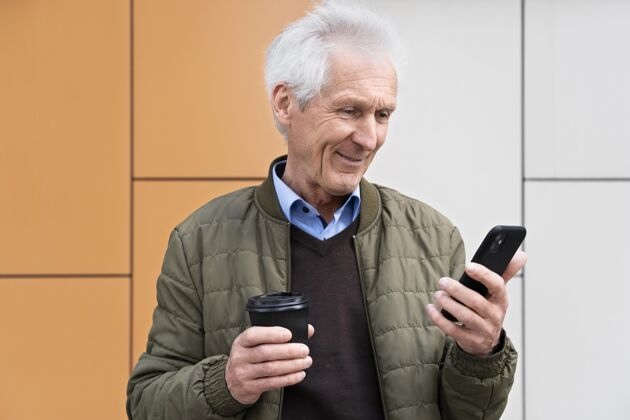 老年笑笑城里的老人一边喝咖啡一边用智能手机城市老年人老年人