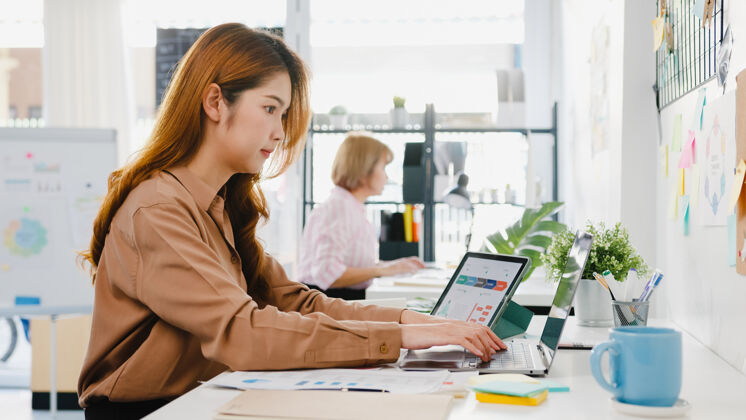 财务年轻的亚洲女企业家社会距离在新的正常情况下病毒预防 而使用笔记本电脑和平板电脑回到办公室工作团队面试文案