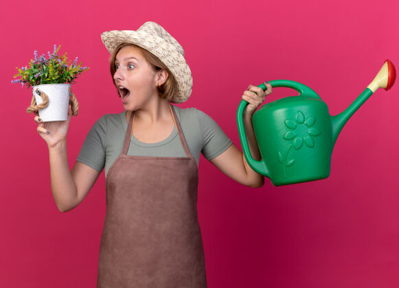 浇水年轻的斯拉夫女园丁戴着园艺帽 拿着浇水罐 看着花盆里的花 惊讶不已举行穿斯拉夫