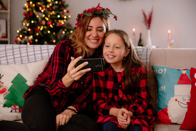 微笑笑眯眯的母女俩坐在沙发上看着手机 在家里享受圣诞节时光沙发女儿圣诞节