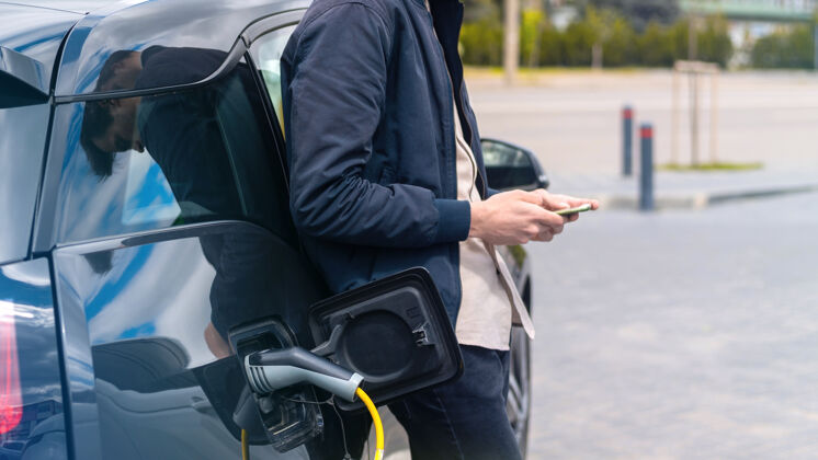 电源男人在充电站给他的电动车充电 用智能手机混合动力环境汽车
