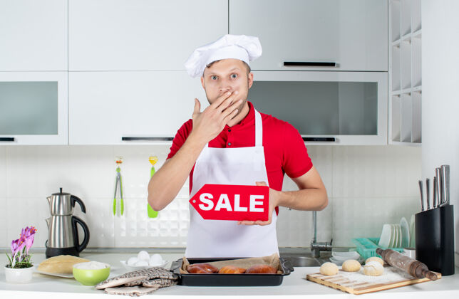 男人在白色厨房里 年轻惊讶的男厨师展示销售标志的俯视图工人年轻成人