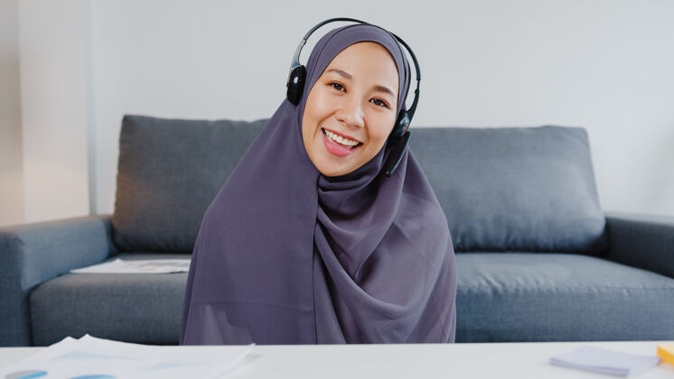 社交亚洲女士戴着耳机用笔记本电脑在客厅远程工作时 在视频电话会议上和同事谈论计划会议年轻人网络