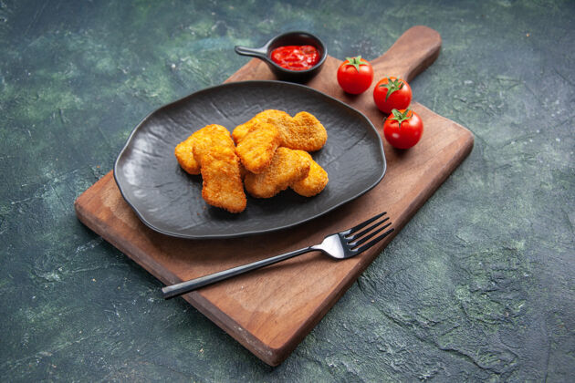 正餐鸡块放在一个黑色的盘子里 叉子放在木板上 番茄酱放在黑暗的表面上 有自由空间面包晚餐叉子