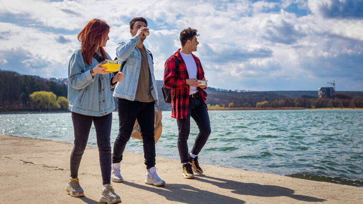 散步三个年轻的朋友在湖边散步 在公园里吃喝树胡同公园
