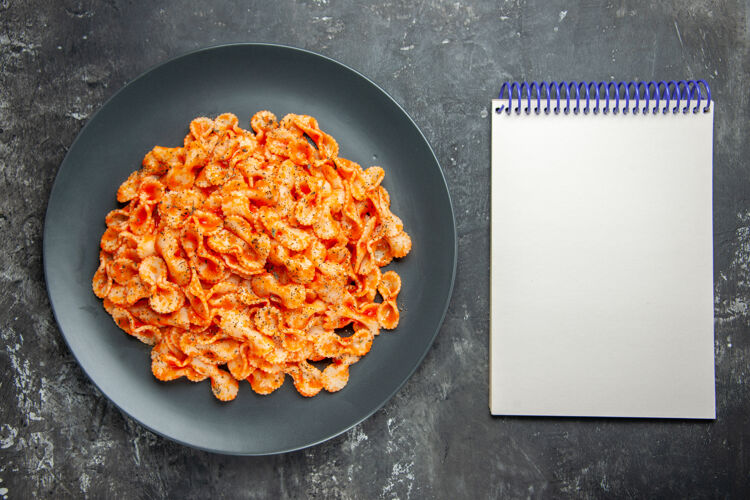 晚餐上图：美味的意大利面食放在黑色盘子里作为晚餐 笔记本放在深色背景上厨具盘子背景