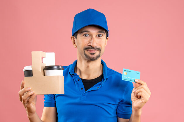 微笑半身镜头 微笑的男送货员戴着帽子拿着订单和银行卡持有工作人