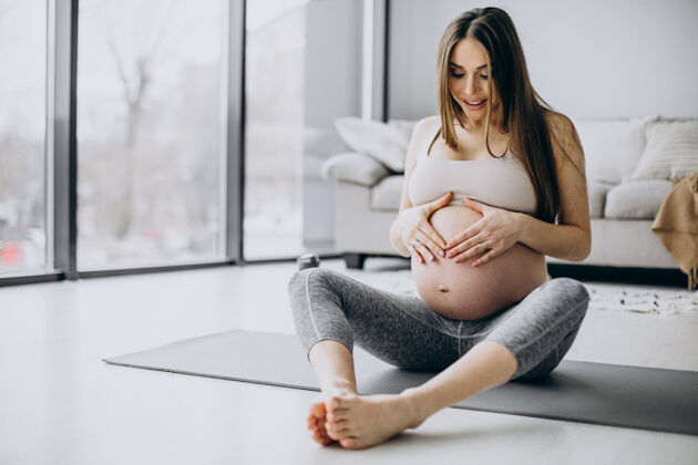 腹部孕妇在家里的垫子上练习瑜伽身体腹部怀孕