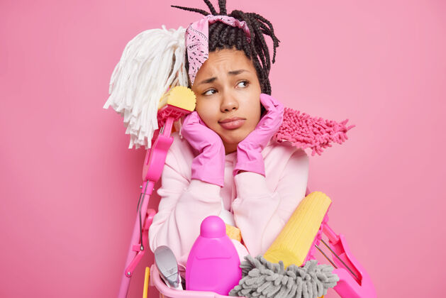 保护一个留着长发绺的男人用清洁用品围住下巴 把一盆洗好的衣服隔在粉红色的地板上手套洗涤剂橡胶