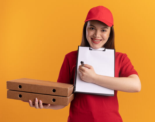 披萨身着制服 面带微笑的漂亮送货员拿着比萨饼盒 用记号笔在剪贴板上写字橘子拿着送货