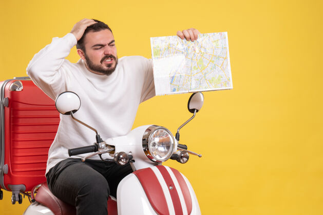 微笑顶视图混乱的家伙坐在摩托车上 手提箱上拿着地图孤立的黄色背景手提箱摩托车车辆