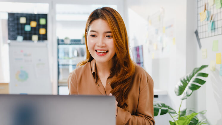 年轻人亚洲女商人社交距离在新常态下使用笔记本电脑进行病毒预防在办公室向同事演示视频通话计划会议远程工作办公室