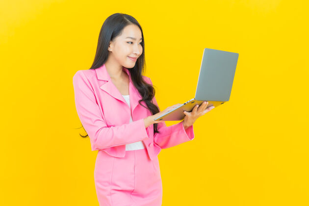 商务女性一幅美丽的亚洲年轻女子微笑的画像 黄色的隔离墙上挂着一台笔记本电脑女士中文工作