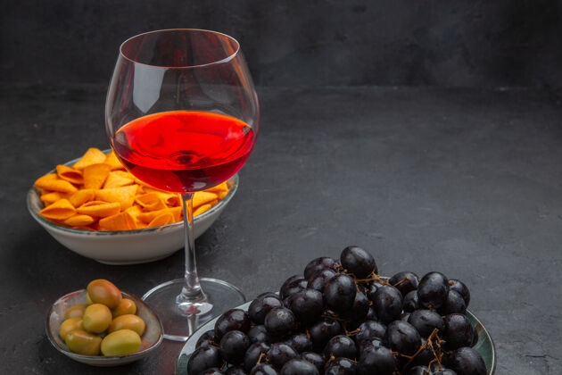 水果侧视图美味的红酒在一个玻璃酒杯和各种小吃的黑色背景红酒各种葡萄酒