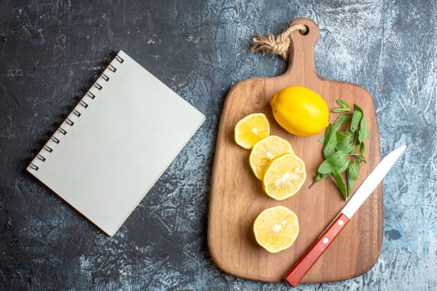 一餐上图：黑色背景下 笔记本旁边的木质砧板上摆放着新鲜柠檬和薄荷刀新鲜刀胡椒