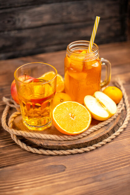 果汁有机新鲜果汁在一个瓶子和玻璃垂直视图与管和水果在一个砧板和棕色的木桌上切割管板