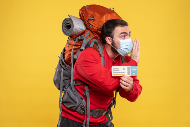人年轻专注的旅行者 戴着医用面罩 背着背包 手里拿着一张黄色的机票人男性肖像