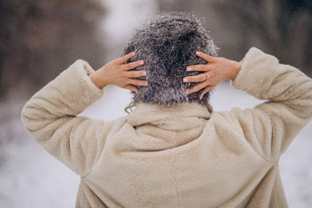 毛衣女人从后面摆姿势 在冬季公园散步美丽帽子自然