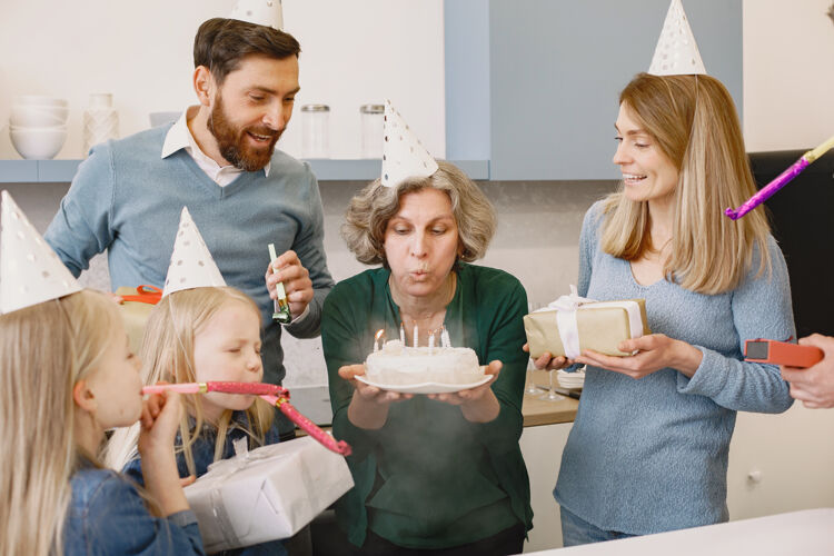 服装一家人和两个女儿一起庆祝祖母的生日 老太太吹灭蜡烛庆祝奶奶女孩