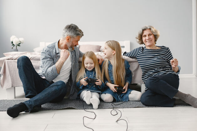 放松快乐的祖父母和两个孙女一家人玩电子游戏坐在地板上游戏世代视频