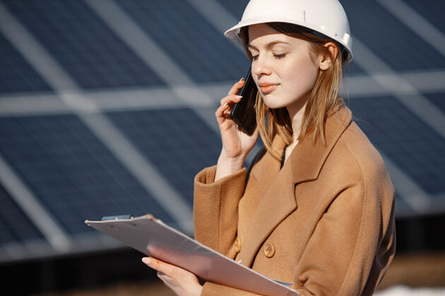 工程师太阳能站年轻的女工程师在工厂工作她在打电话和做生意戴着头盔拿着文件的女人电压电池技术员
