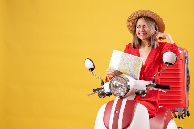 成人骑着轻便摩托车的漂亮女孩 带着红色手提箱 把地图合上耳朵人坐着地图